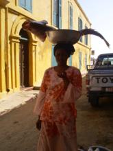 A woman carrying a fish in a bowl on her head